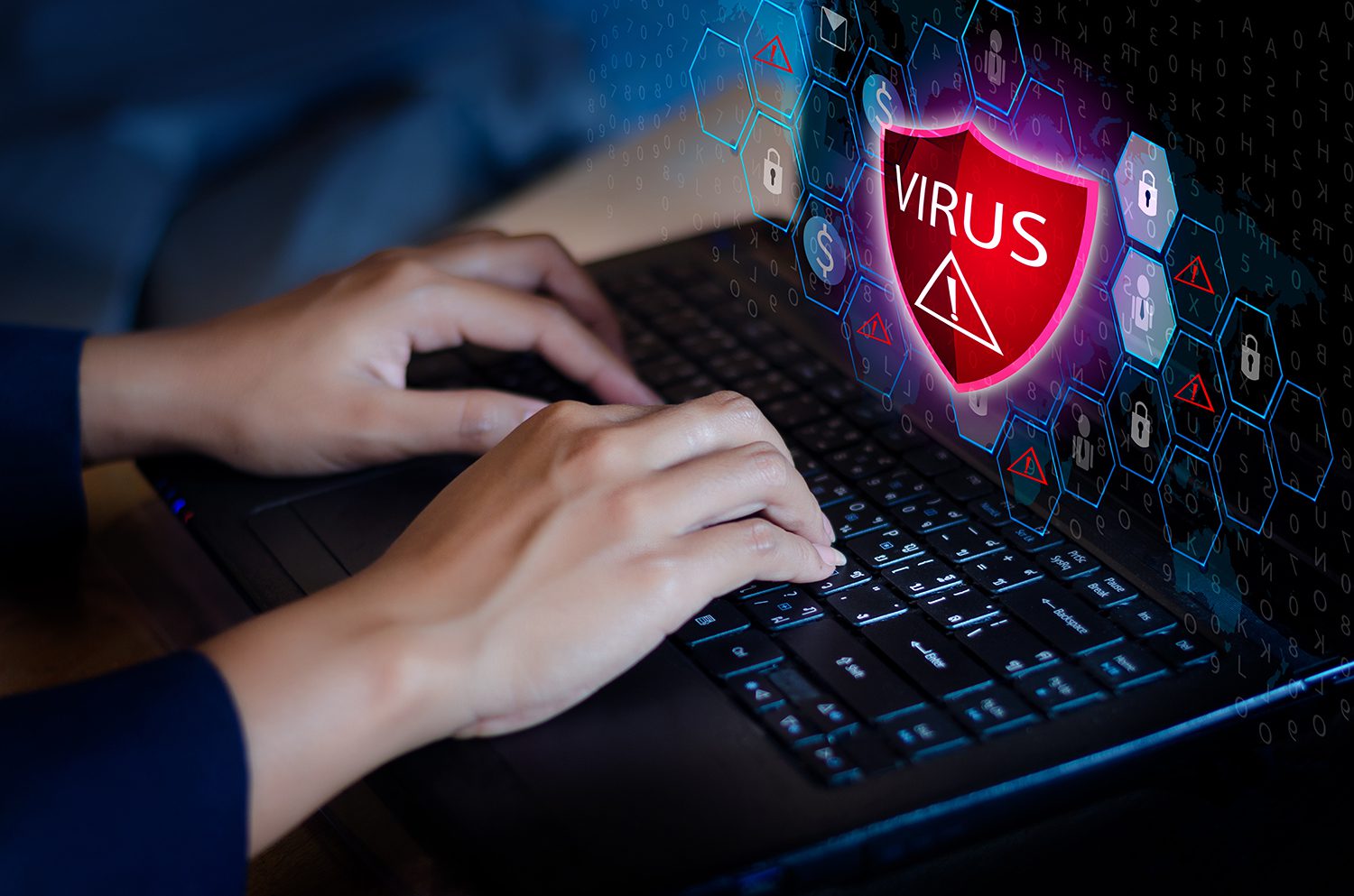 A person typing on a laptop with a big red shield that says "VIRUS" on the screen.